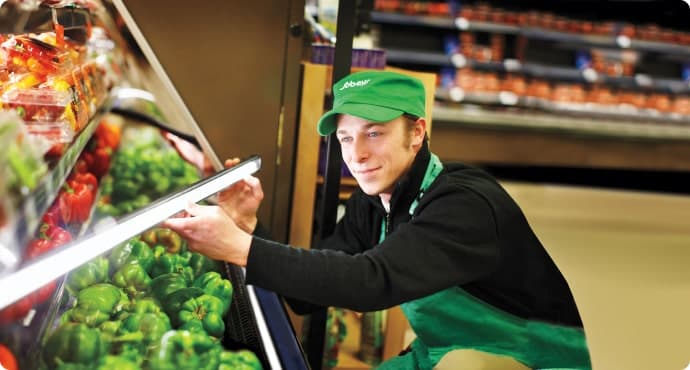 An image of a Sobeys teammate arranging all the vegetables and the lights of the vegetable section.