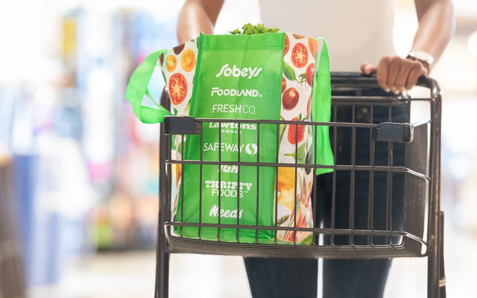 An image of a man carrying sobeys bag filled with fruits and vegetables in a trolley.