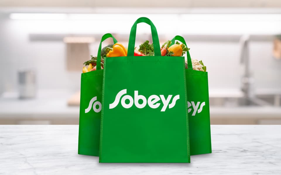 An image of a man carrying sobeys bag filled with fruits and vegetables in a trolley.